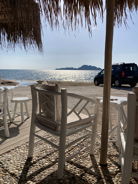 weiße Holzstühle und Bast Sonnenschirme mit Blick aufs Meer