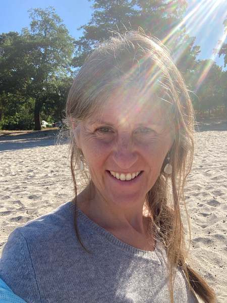 Frau mit grauem Pullover am Strand mit Sonnenstrahlen auf dem Kopf die aussteigen wird