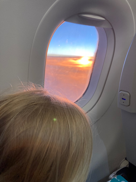 Hinterkopf von blondem Kind und Blick aus dem Flugzeugfenster auf den Sonnenuntergang